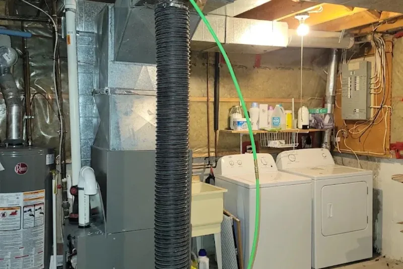 Vacuum hose and cleaning line running into the ductwork above a basement furnace