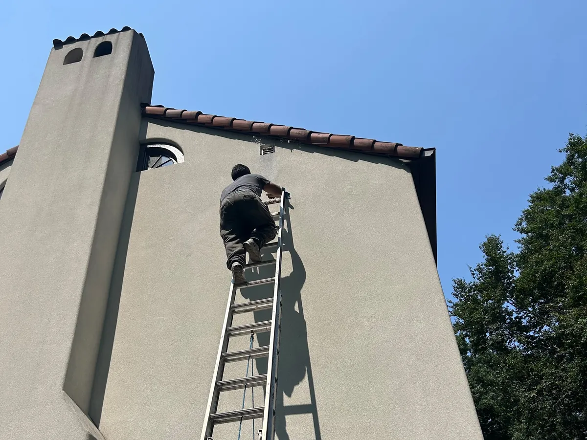Technician on an extension ladder reaching an exterior dryer vent
